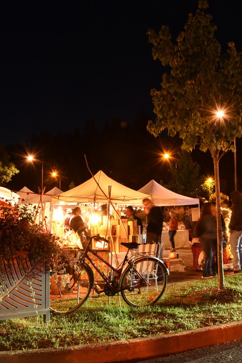 Marché nocturne éclairé avec vélo et arbres.