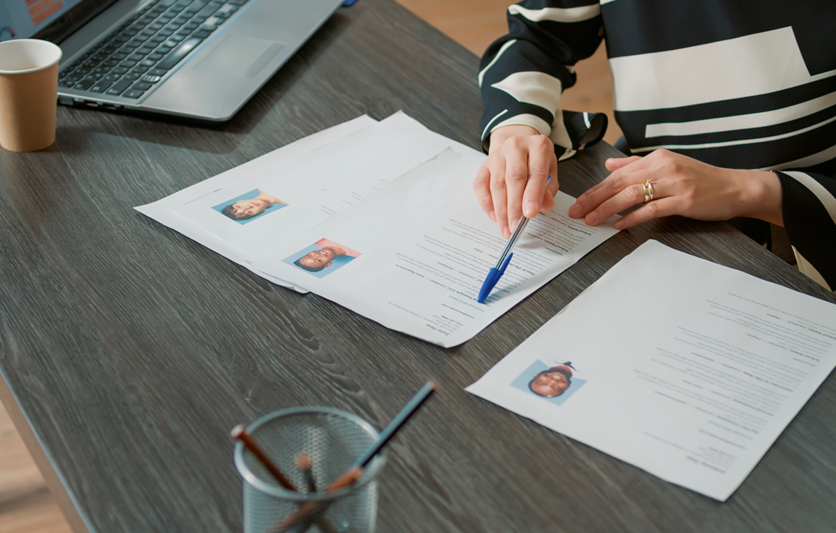 Personne examinant des CV avec photos sur un bureau.