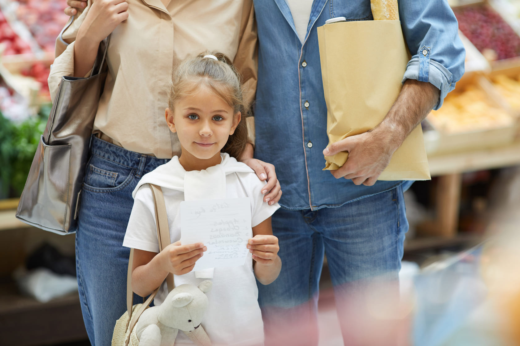 Fille tenant liste courses avec parents au marché.